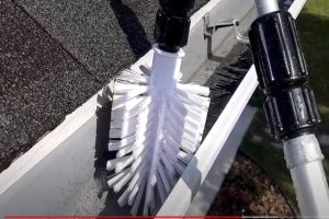 Roofing worker using a brush for gutter cleaning